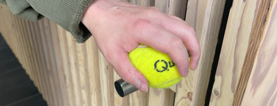 Nærbillede af hånd på tennisbold på gelænderet